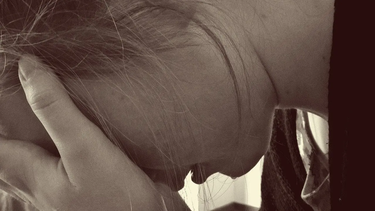 A sad young woman holding her head in her hands - Support Your Teen Through a Breakup