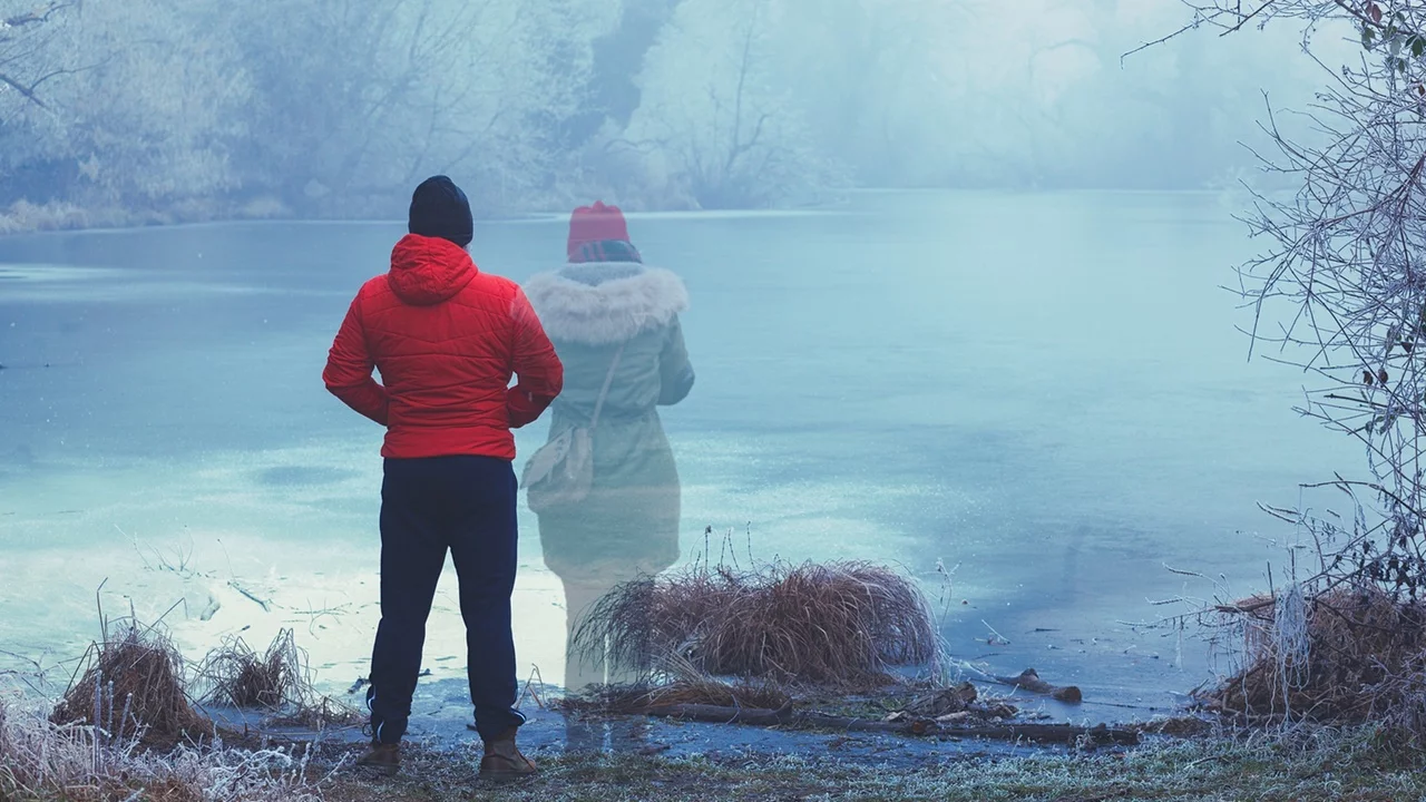 Lonely man in red jacket standing by the lake in winter, with transparent woman figure standing next to him - loss - All is Well