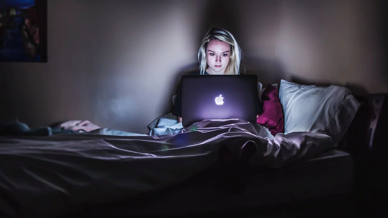 a woman looking at her laptop, receiving online therapy from her bed